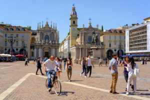 PIazza San Carlo em Turim, com pessoas caminhando e passeando de Bicicleta, num dia de céu azul