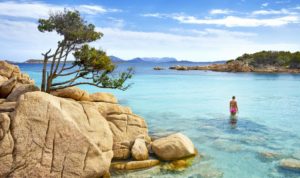 Mulher dentro de um mar azul transparente, com rochas em primeiro plano, na Costa Smeralda, Sardenha