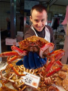 Homem segurando crustáceo e sorrindo para a câmera no mercado de Rialto, em Veneza