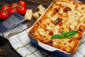Lasanha em um prato grande, com tomates e queijo parmigiano ao lado, comidas típicas italianas.