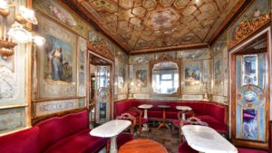Interior do Caffe Florian em Veneza, com mesas elegantes, sofas e pinturas no teto