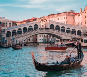 Casal passeando de gôndola em Veneza, ao pôr do Sol e com Ponte Rialto ao fundo