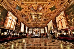 Vista de uma grande sala na Scuola Grande di San rocco, em Veneza, com piso e paredes decorados, e pinturas de Tintoretto