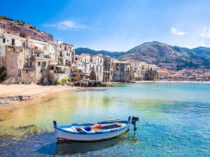Cefalu na Sicília, Itália, com casas claras, mar azul e braco em primeiroplano