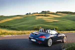 Green gentle hills and a blue convertible car on a road in Tuscany, Italy