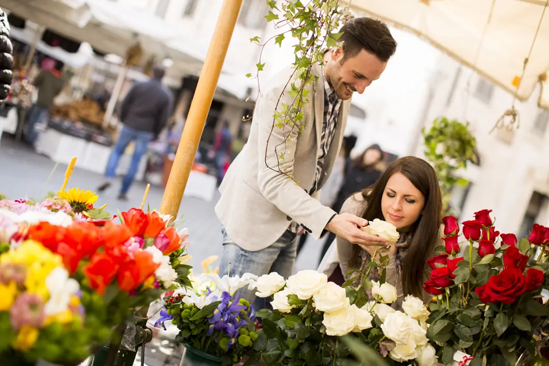 Smiling couple picking fresh flowers at an open-air market in Tuscany during spring