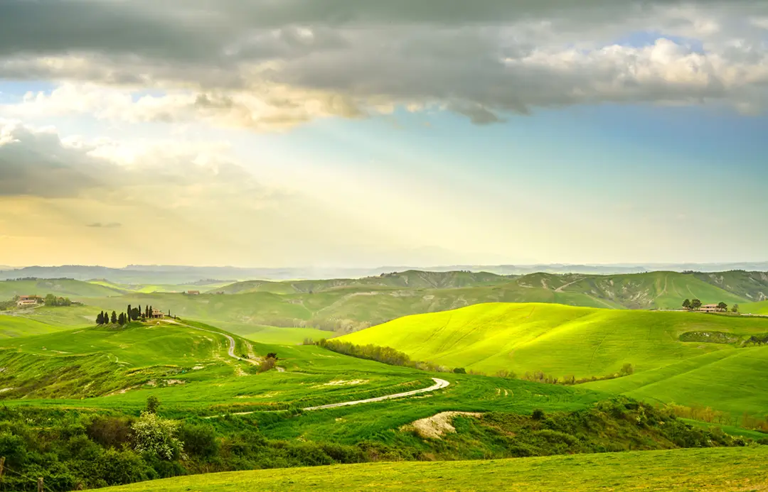 Lush green landscape with rolling hills and typical houses in the Tuscany region, Italy.