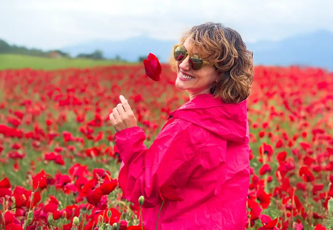 Smiling woman in a pink coat in a blooming field of red poppies in Tuscany during spring