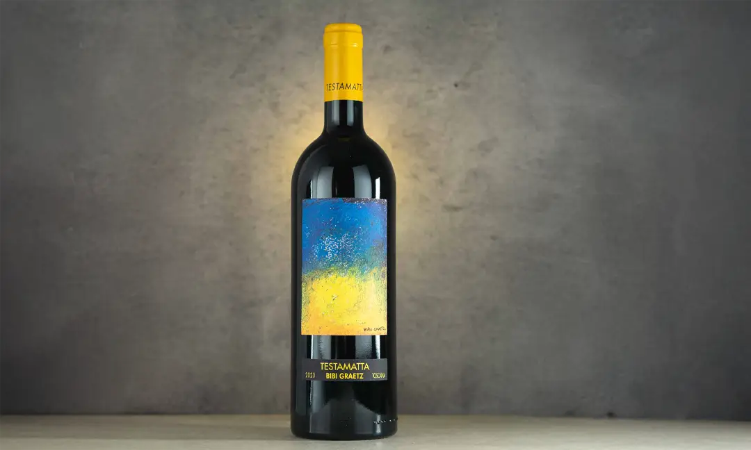 Garrafa de vinho tinto Bibi Graetz Testamatta 2020 com rótulo artístico em azul e amarelo, destacada contra fundo neutro, representando um dos ícones dos vinhos da Toscana.